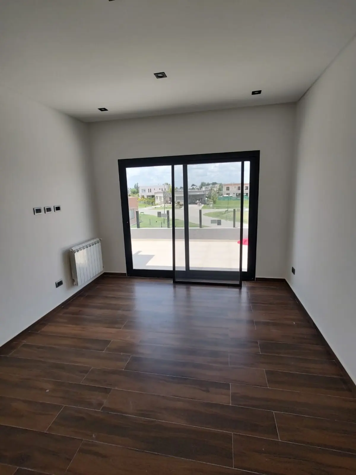 Sala de estar moderna com piso de madeira escura e janelas amplas — projeto Casa En El Barrio De Los Talas, por Ves Arquitectura, em Canning